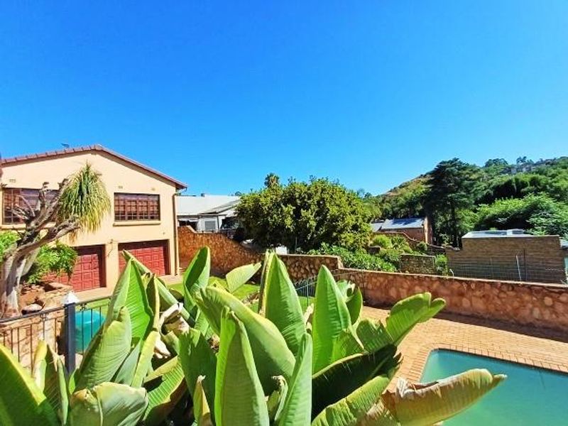 Rear exterior view featuring a swimming pool, paved patio area, stone retaining wall, and a double garage with a tiled roof.