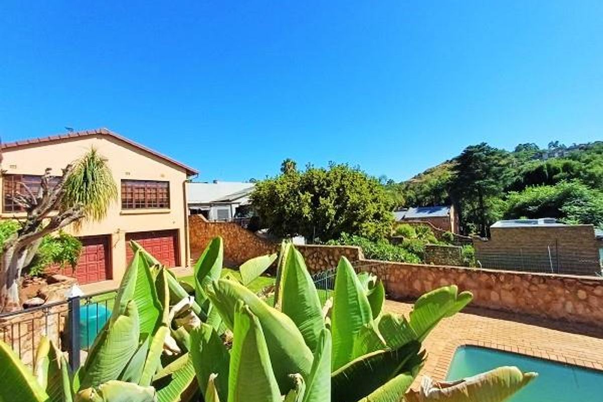 Rear exterior view featuring a swimming pool, paved patio area, stone retaining wall, and a double garage with a tiled roof.