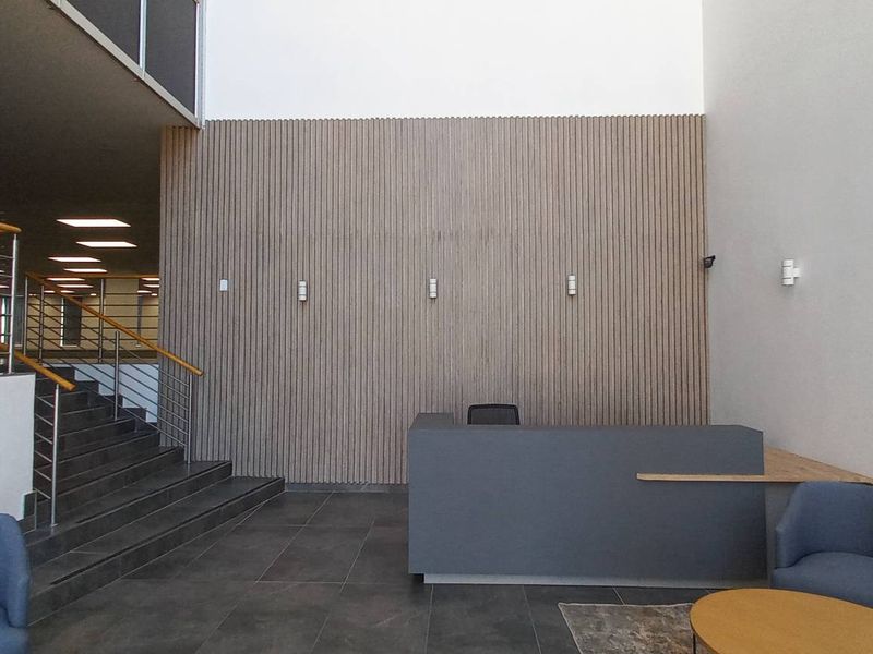 Modern office reception area featuring a striking slatted timber feature wall, tiled flooring, and a contemporary staircase with stainless steel balustrades.