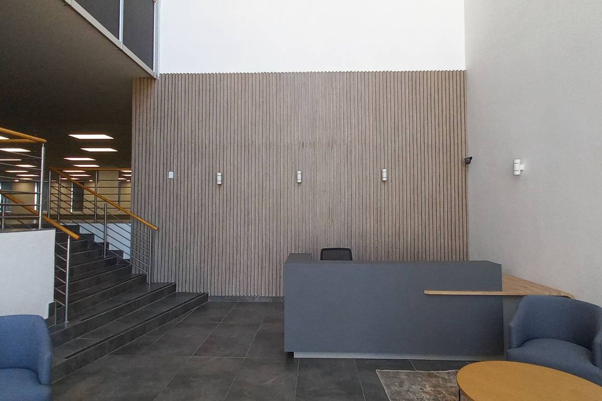 Modern office reception area featuring a striking slatted timber feature wall, tiled flooring, and a contemporary staircase with stainless steel balustrades.