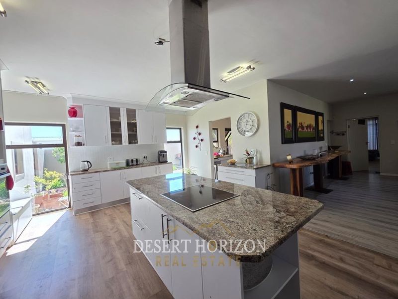 Modern open-plan kitchen featuring a central island with granite countertops, built-in hob, stainless steel extractor fan, and ample white cabinetry.