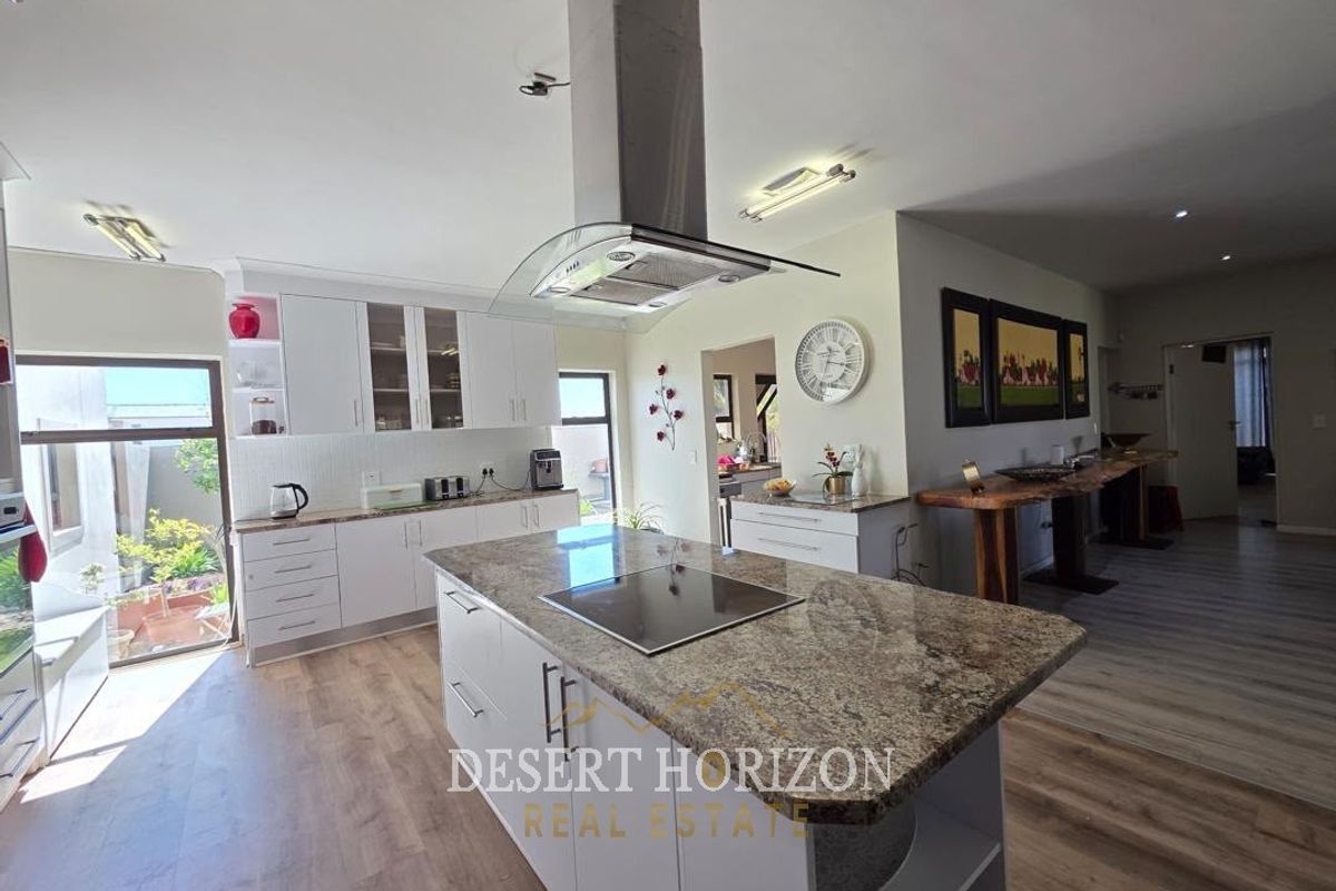 Modern open-plan kitchen featuring a central island with granite countertops, built-in hob, stainless steel extractor fan, and ample white cabinetry.