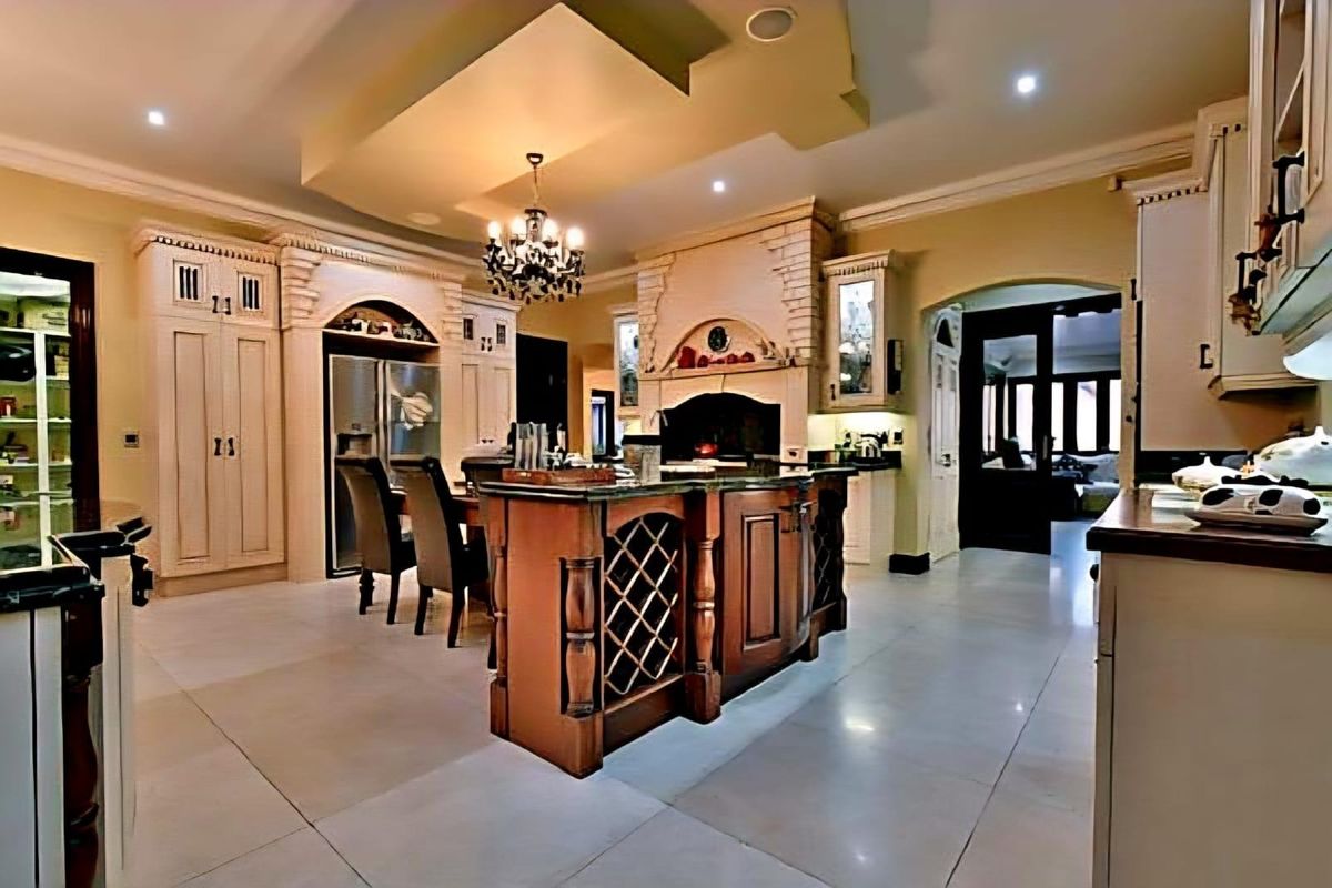 Spacious kitchen featuring a large central island with integrated wine storage, custom cabinetry, stone-look flooring, and a decorative range hood.