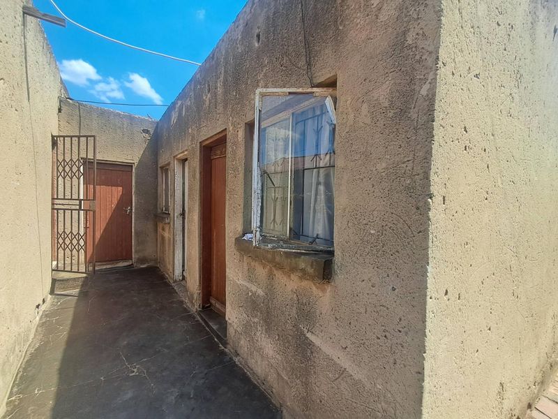 Rear exterior view of the property showing weathered plaster walls, security gates, and metal window frames with visible signs of wear.