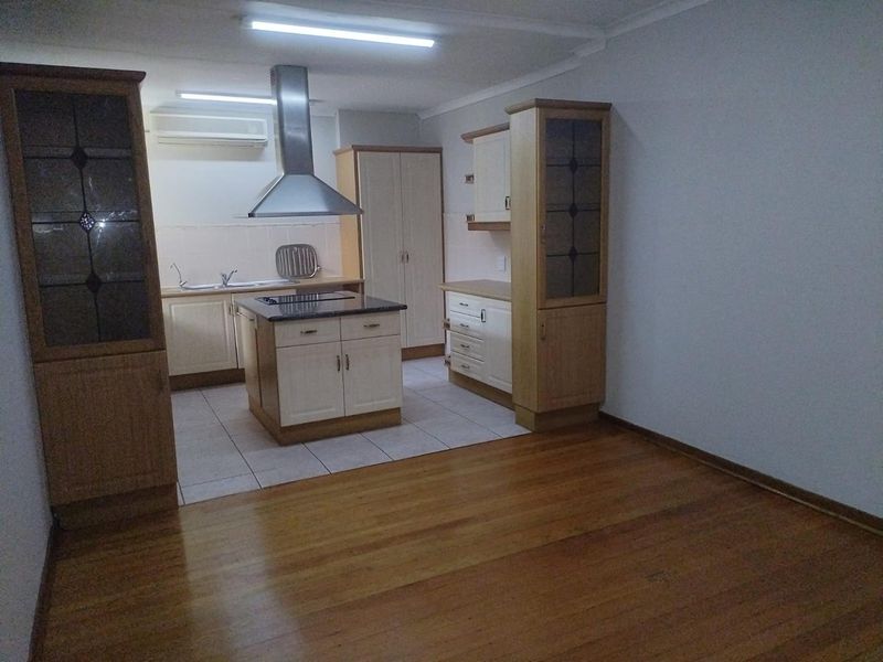 A spacious kitchen featuring a central island, built-in cabinetry, extractor fan, and a combination of tiled and timber flooring.