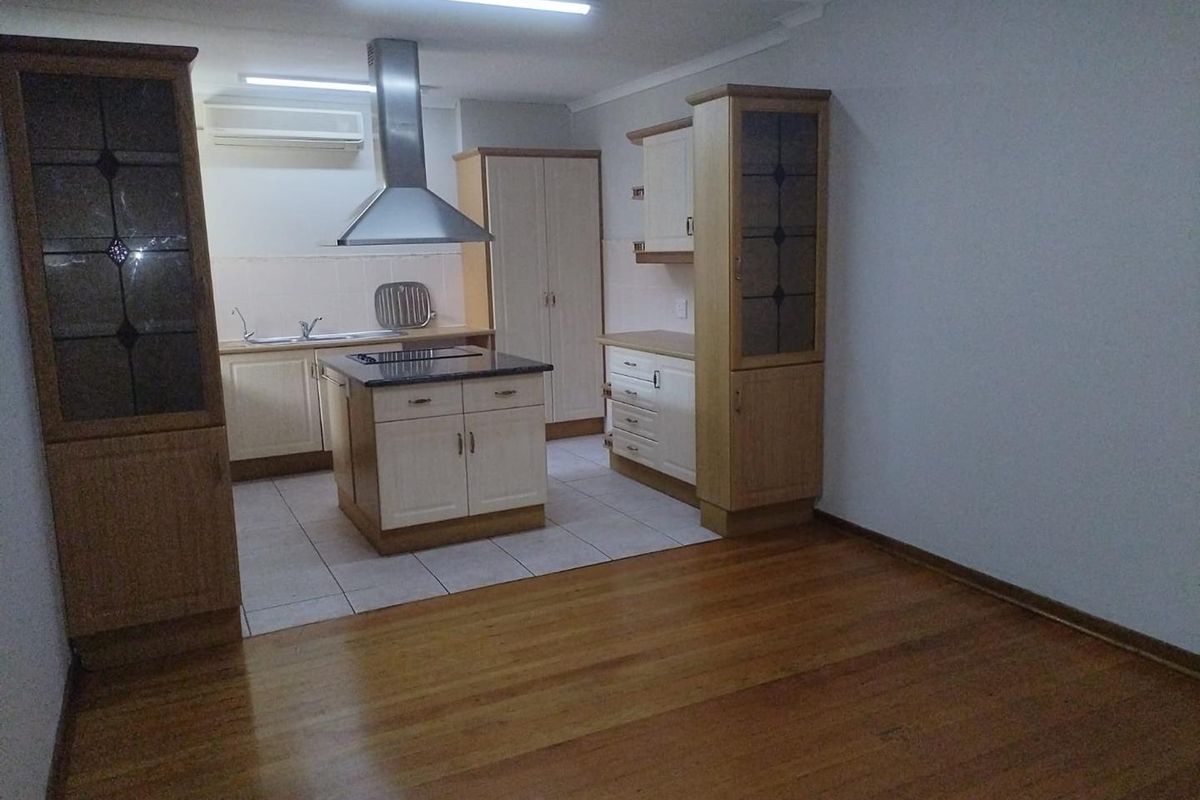 A spacious kitchen featuring a central island, built-in cabinetry, extractor fan, and a combination of tiled and timber flooring.