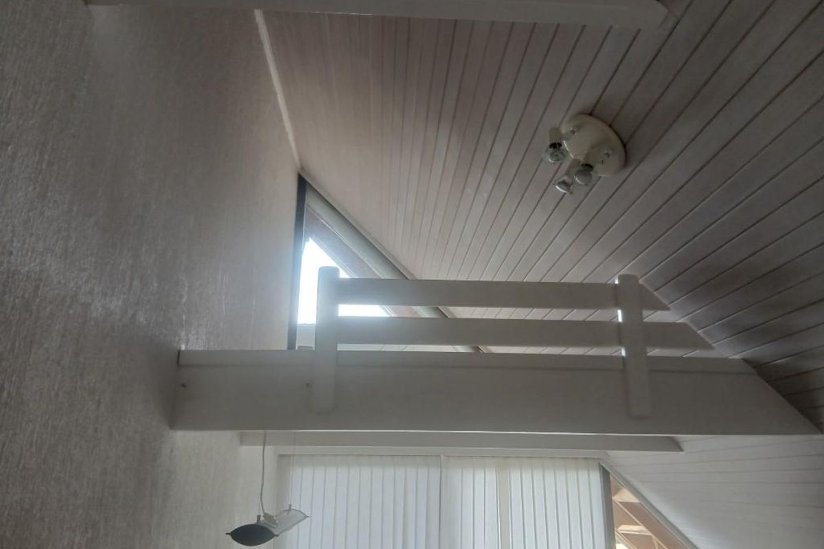 A loft area featuring a raked timber-clad ceiling, a built-in safety railing, and a triangular window providing natural light.