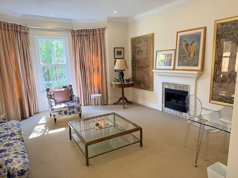 A well-maintained living room featuring a fireplace with a tiled surround, recessed lighting, and a large sash window with elegant drapery.
