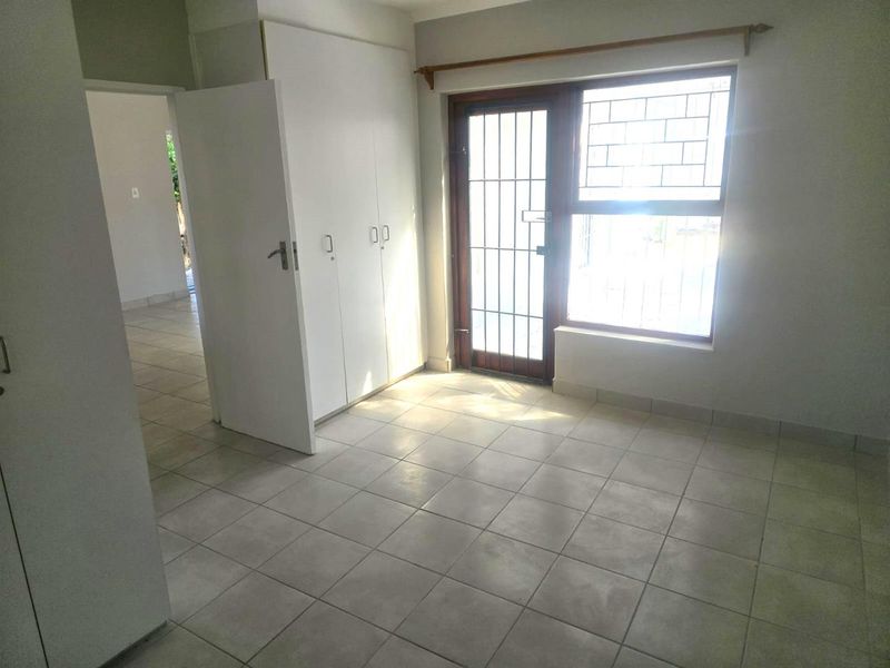 A bright, empty bedroom featuring tiled flooring, built-in cupboards, and a secure door leading to the exterior.