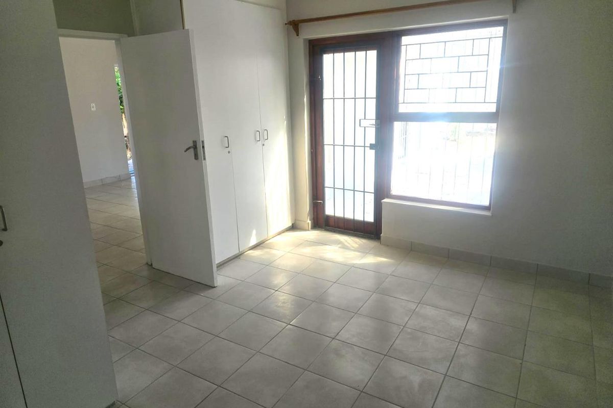 A bright, empty bedroom featuring tiled flooring, built-in cupboards, and a secure door leading to the exterior.