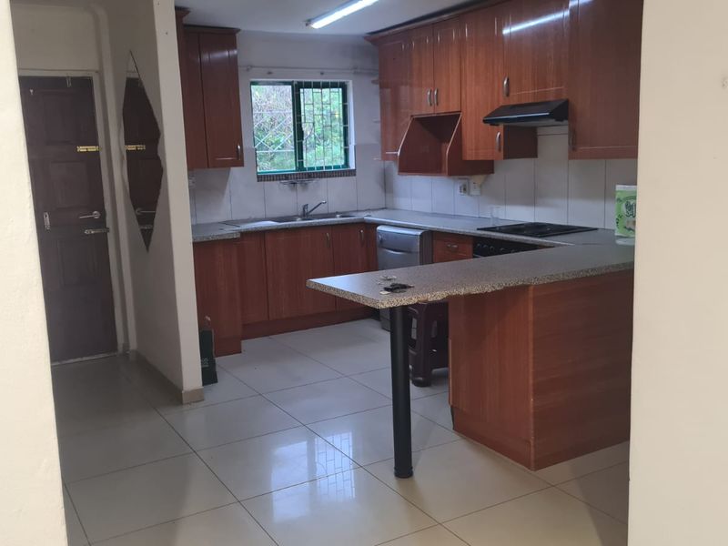 A functional kitchen featuring wood-look laminate cabinetry, granite-style countertops, a built-in hob with extractor fan, and tiled flooring.