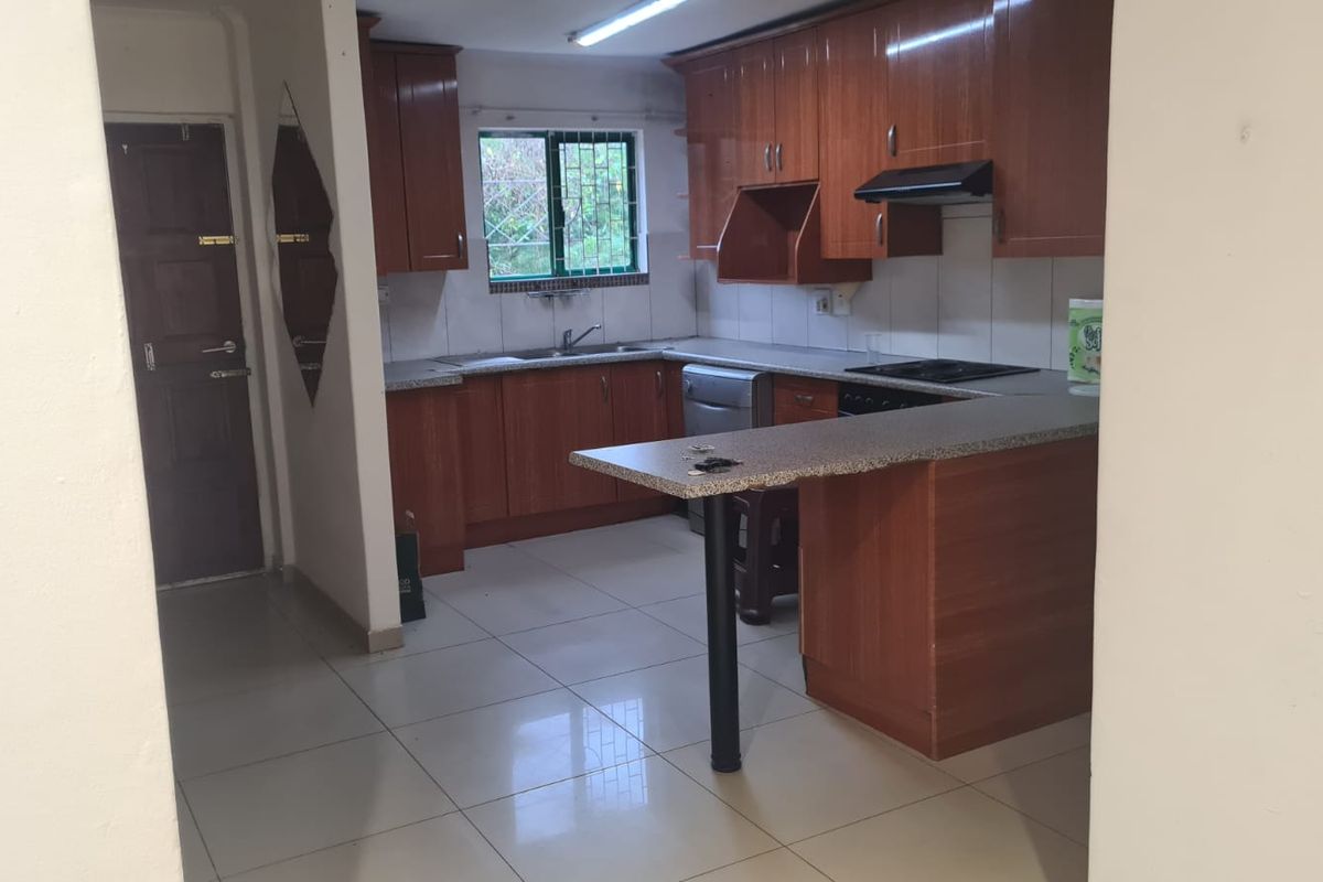 A functional kitchen featuring wood-look laminate cabinetry, granite-style countertops, a built-in hob with extractor fan, and tiled flooring.