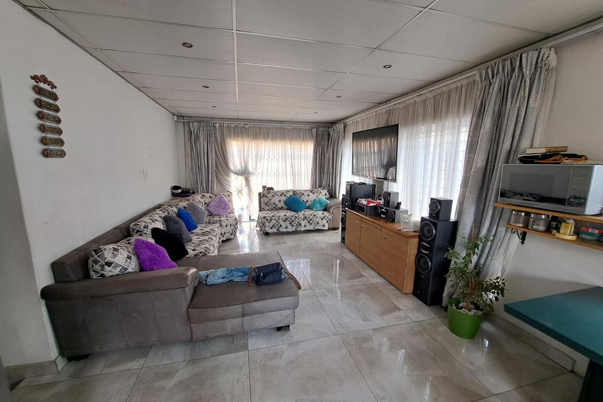 A living room featuring large format floor tiles, recessed ceiling lighting, and floor-to-ceiling curtains covering the window and door areas.