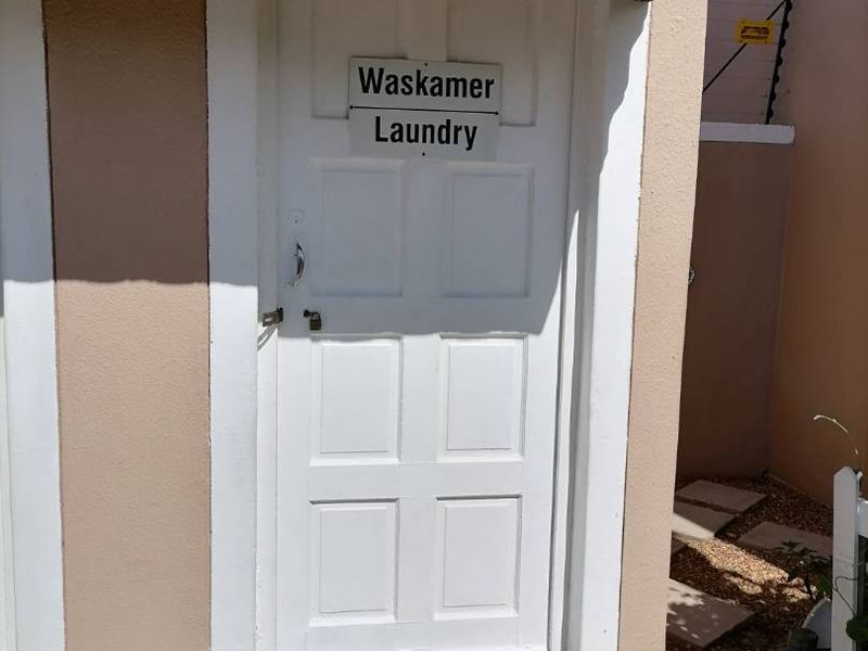 Exterior view of a dedicated laundry room entrance featuring a tiled awning and security fencing.