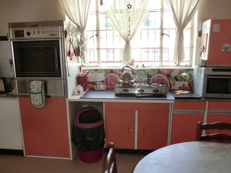A dated kitchen featuring original cabinetry, a built-in oven, gas hob, and large window with security bars, offering potential for modern renovation.