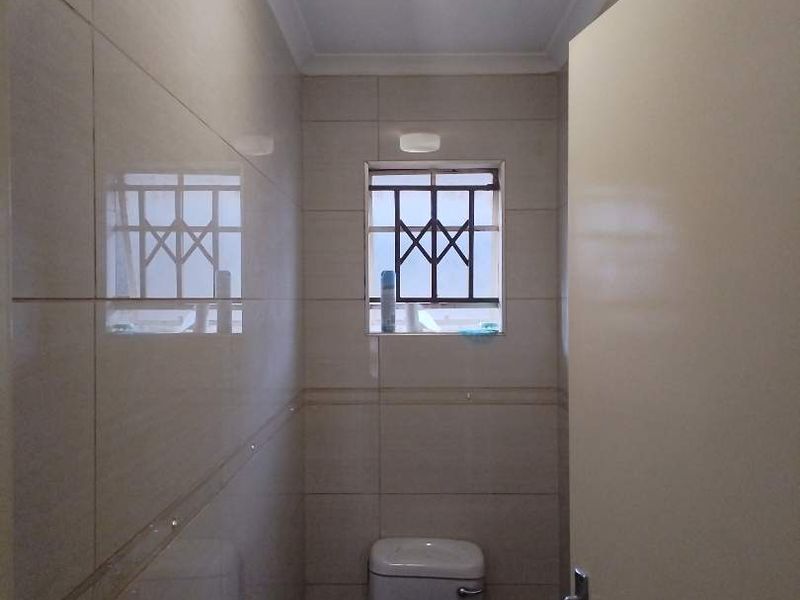 A compact, tiled bathroom featuring a standard flush toilet, security-barred window, and neutral wall finishes.
