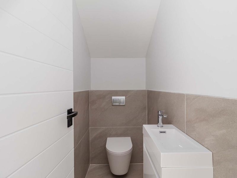 A modern, compact guest bathroom featuring a wall-hung toilet with a concealed cistern and a sleek vanity basin with a mixer tap.