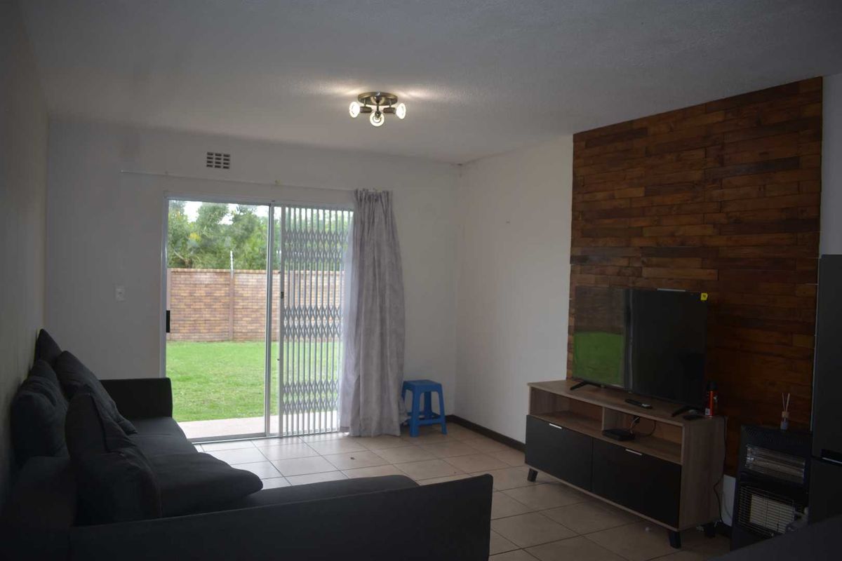 A living room featuring tiled flooring, a decorative wood-paneled feature wall, and sliding glass doors providing access to the garden.
