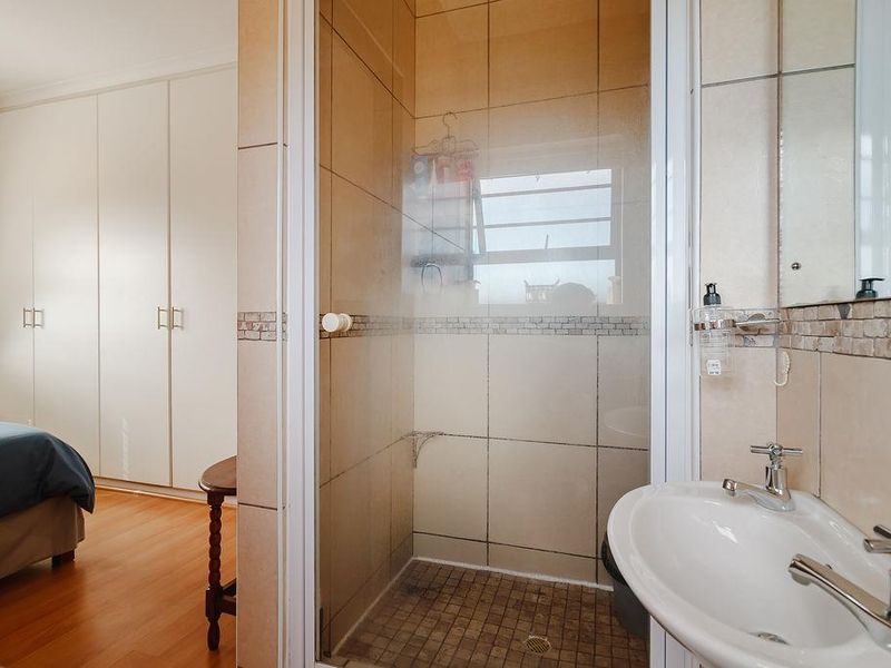 A functional bathroom featuring a shower enclosure with tiled walls, a pedestal basin with chrome taps, and adjacent built-in bedroom cupboards.