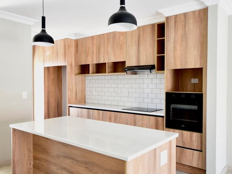 Modern kitchen featuring wood-grain cabinetry, a central island with a stone countertop, subway tile backsplash, and integrated appliances.