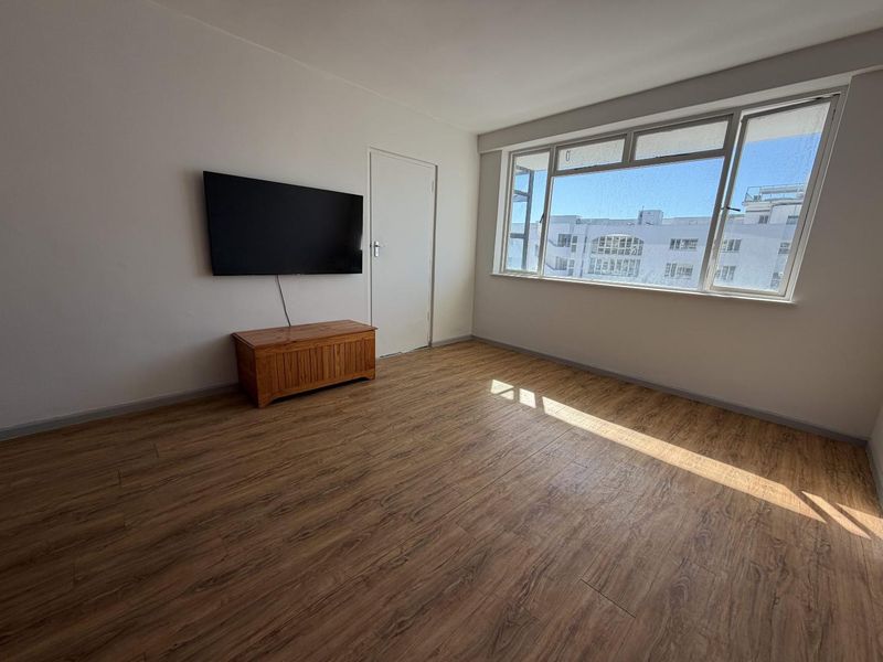 A bright and spacious living area featuring modern laminate flooring and a large window that allows for ample natural light.