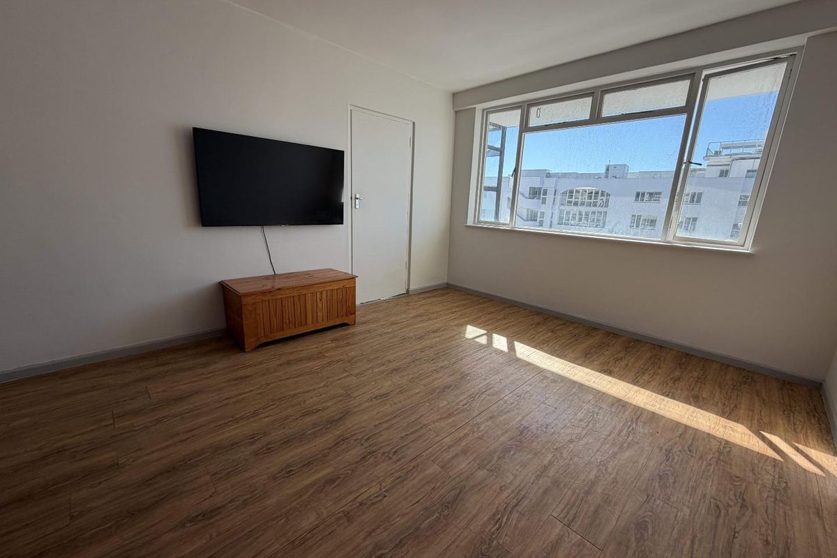 A bright and spacious living area featuring modern laminate flooring and a large window that allows for ample natural light.