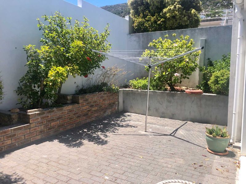A private rear courtyard featuring paved flooring, a brick retaining wall, and established garden beds enclosed by high boundary walls.