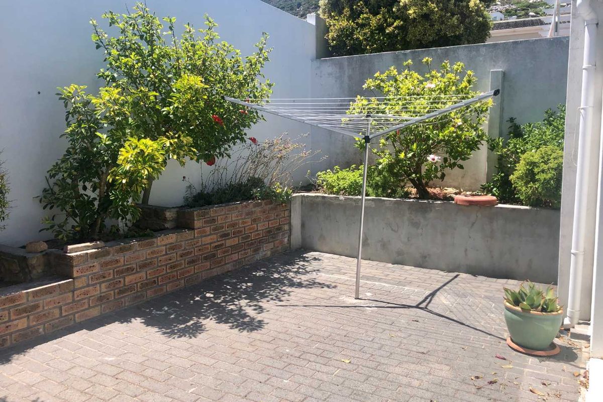 A private rear courtyard featuring paved flooring, a brick retaining wall, and established garden beds enclosed by high boundary walls.
