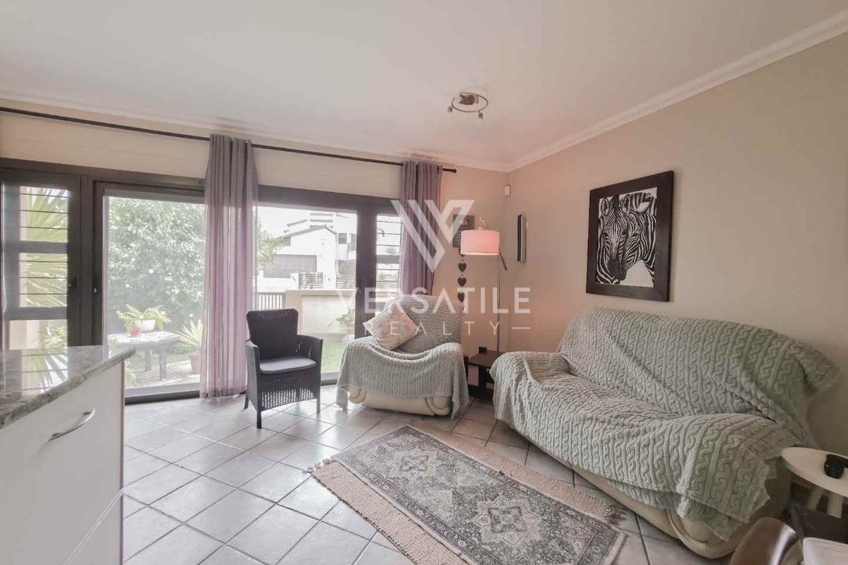 A bright living room featuring tiled flooring and large sliding glass doors that provide direct access to the outdoor garden area.