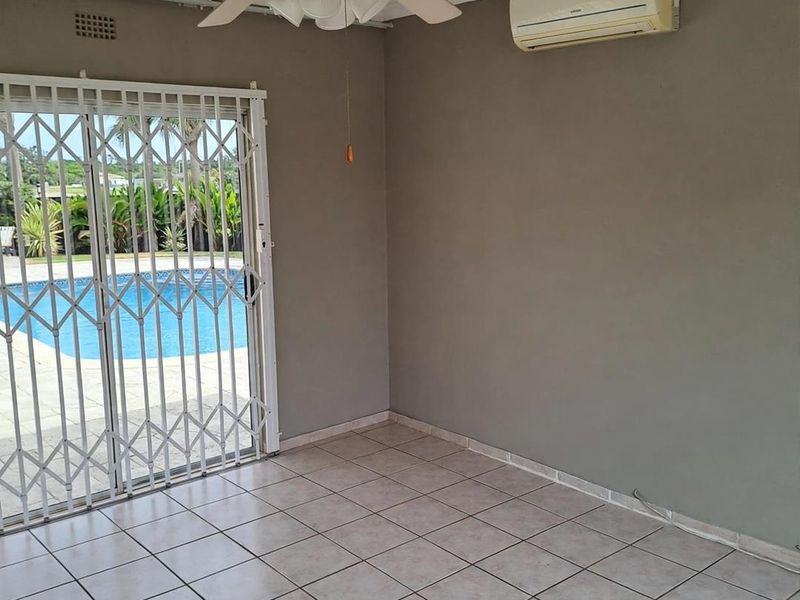 An empty living room featuring tiled floors, a ceiling fan, and a split-system air conditioner, with direct access to the pool area via a security gate.