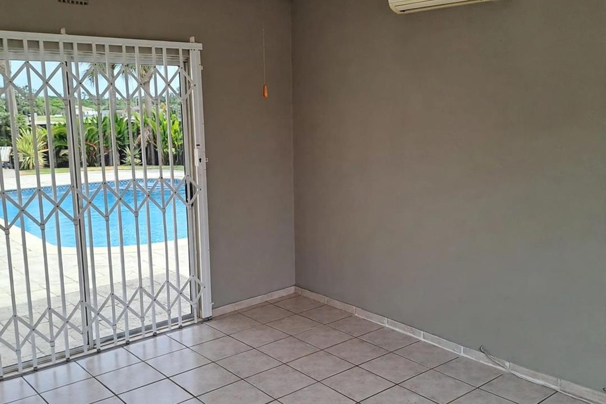 An empty living room featuring tiled floors, a ceiling fan, and a split-system air conditioner, with direct access to the pool area via a security gate.