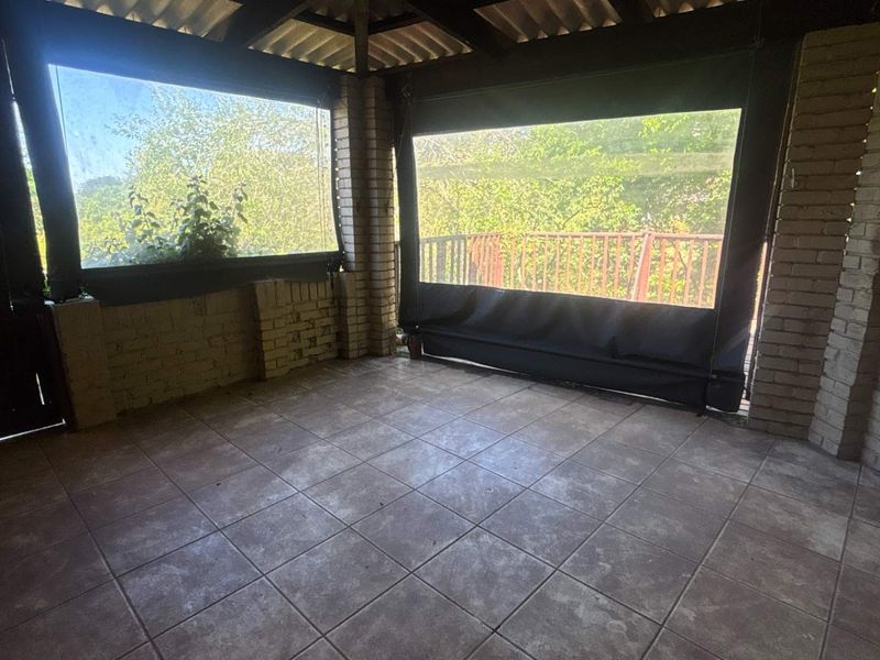 A covered patio area featuring tiled flooring, exposed brick pillars, and protective canvas blinds, offering a functional outdoor space.