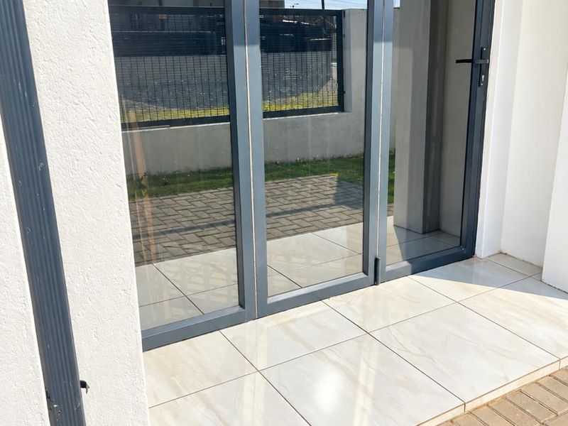 A modern patio area featuring sleek aluminium folding doors and clean tiled flooring, providing a seamless transition to the outdoor paved space.