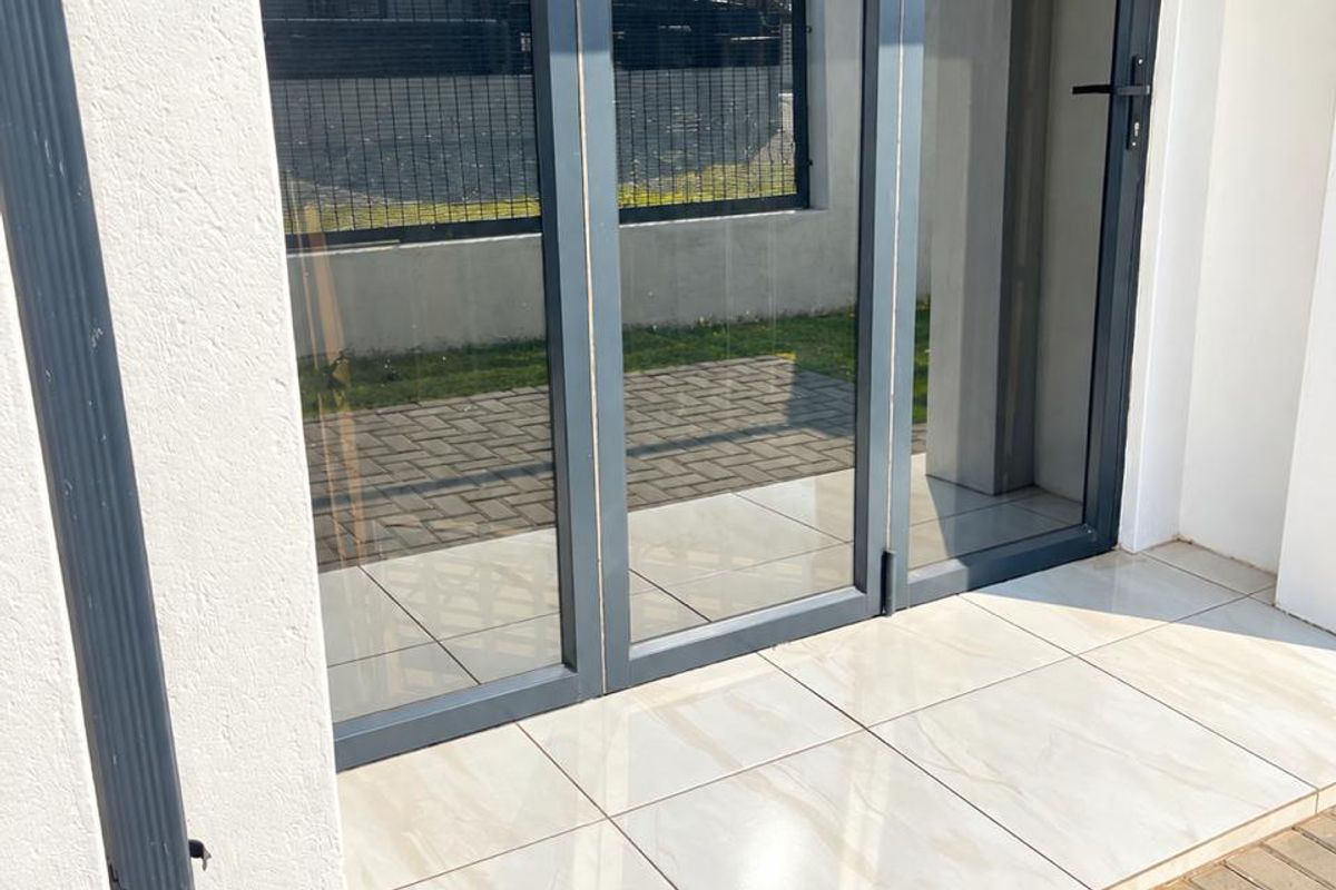A modern patio area featuring sleek aluminium folding doors and clean tiled flooring, providing a seamless transition to the outdoor paved space.