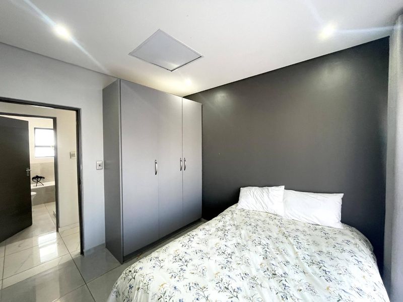 A modern bedroom featuring tiled flooring, a built-in wardrobe, and a dark accent wall, with an adjoining bathroom visible through the doorway.
