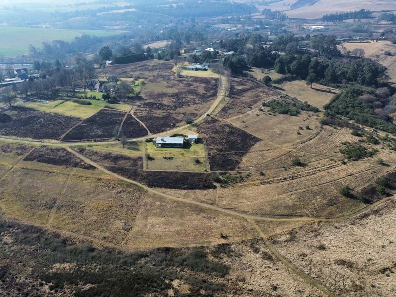 Aerial view of a large residential vacant land plot featuring expansive open fields, natural vegetation, and an existing gravel access road.