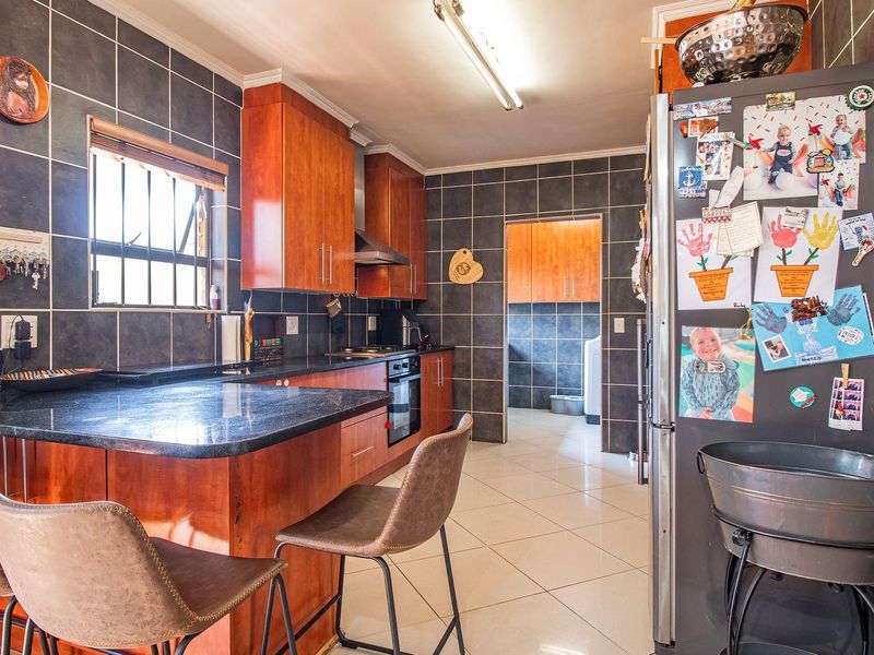 A functional kitchen featuring wood-finish cabinetry, dark granite countertops, tiled walls, and a breakfast bar, with an adjoining scullery area.