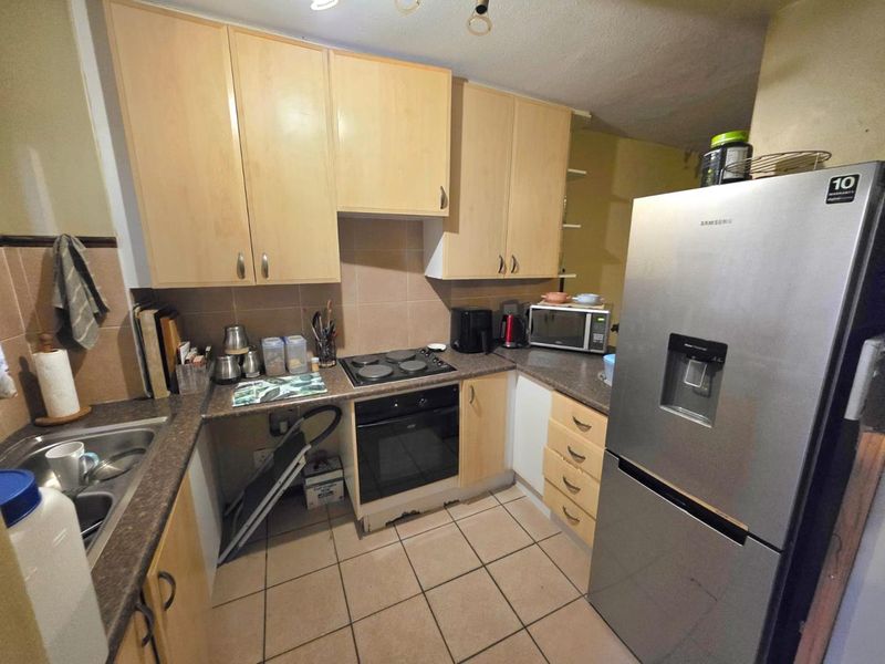 A functional kitchen featuring light wood-tone cabinetry, laminate countertops, tiled backsplash, and built-in cooking appliances with ceramic floor tiles.