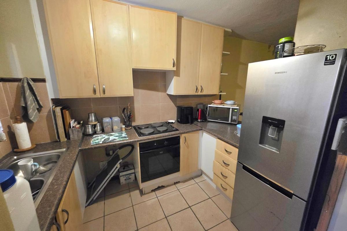 A functional kitchen featuring light wood-tone cabinetry, laminate countertops, tiled backsplash, and built-in cooking appliances with ceramic floor tiles.