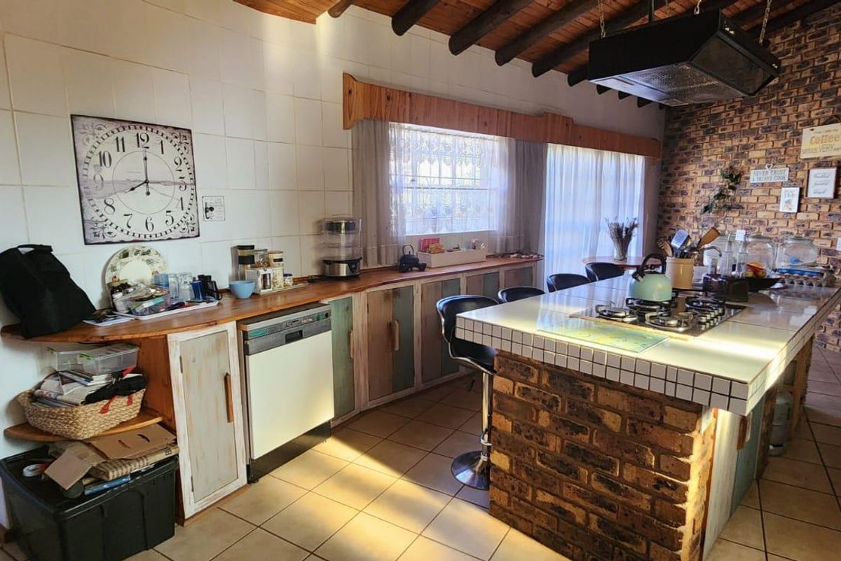 Spacious kitchen featuring a central brick-base island with integrated gas hob, exposed timber beam ceiling, and rustic brick feature wall.