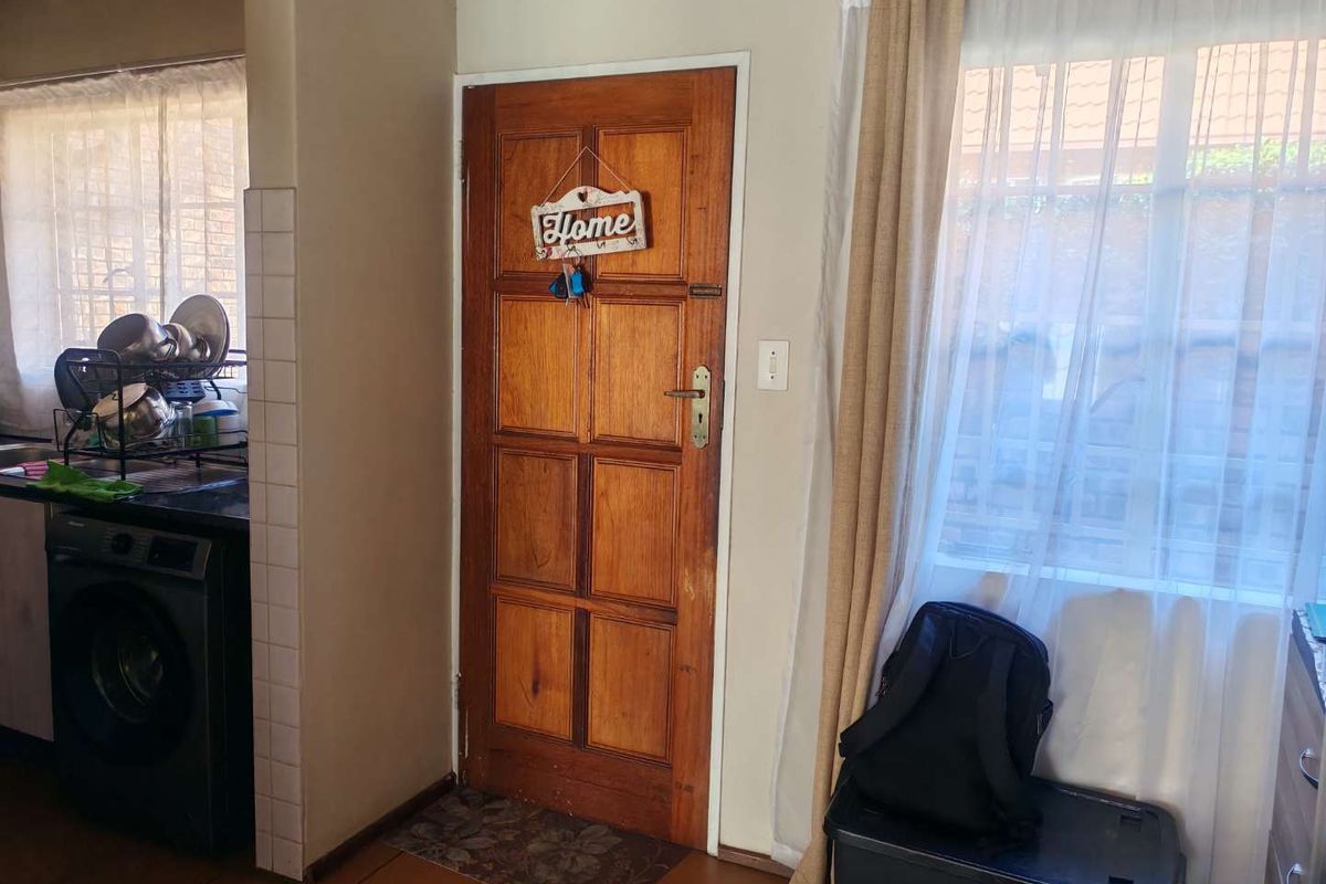 A functional kitchen area featuring tiled flooring, granite countertops, and a traditional timber entrance door with natural light from the adjacent window.