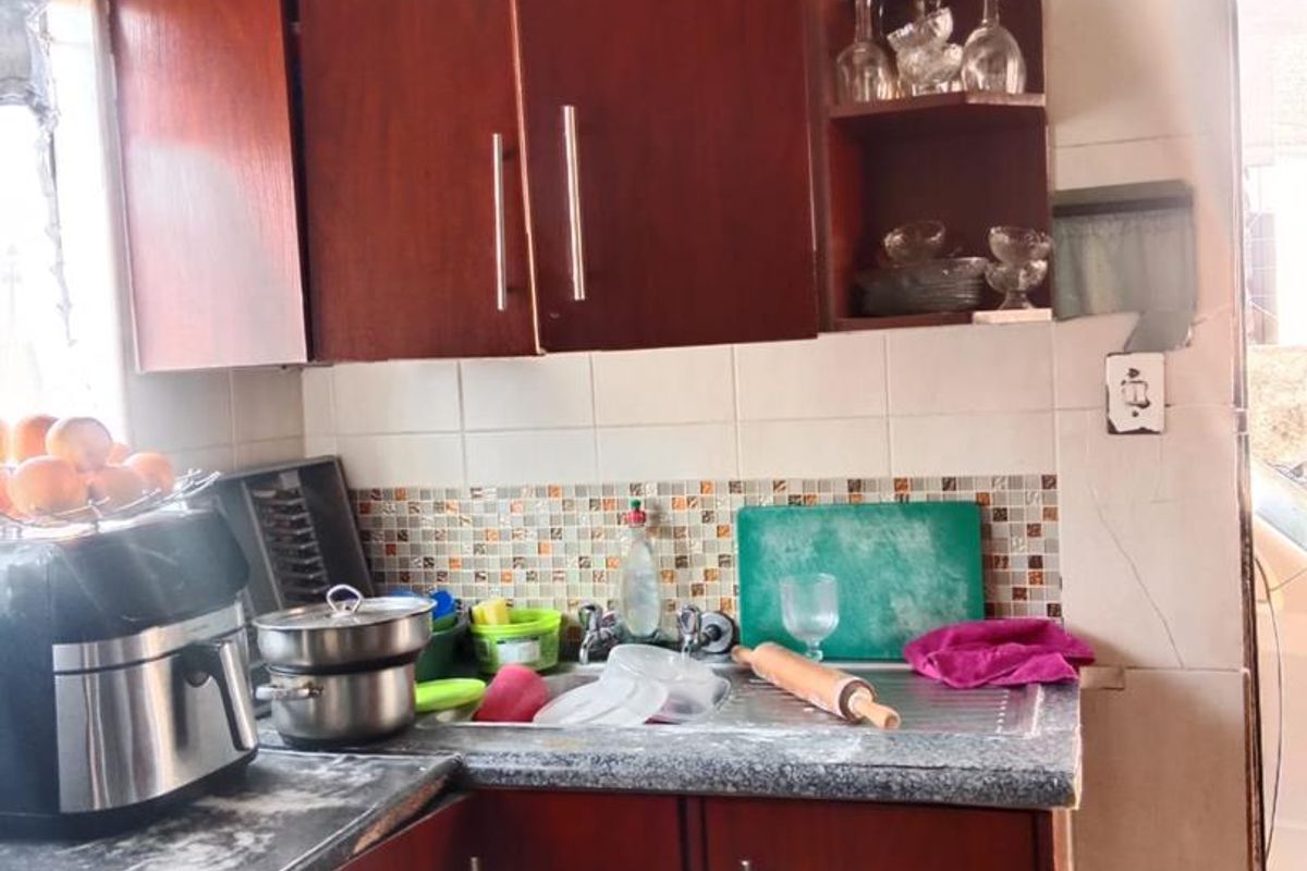 A compact kitchen featuring dark wood-tone cabinetry, tiled backsplash, and laminate countertops, requiring cosmetic updates to modernize the space.