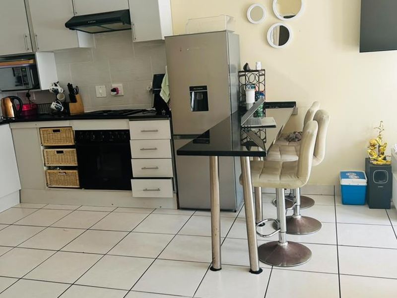 A functional kitchen featuring built-in cabinetry, an integrated oven and hob, extractor fan, and a sleek black breakfast bar with tiled flooring throughout.