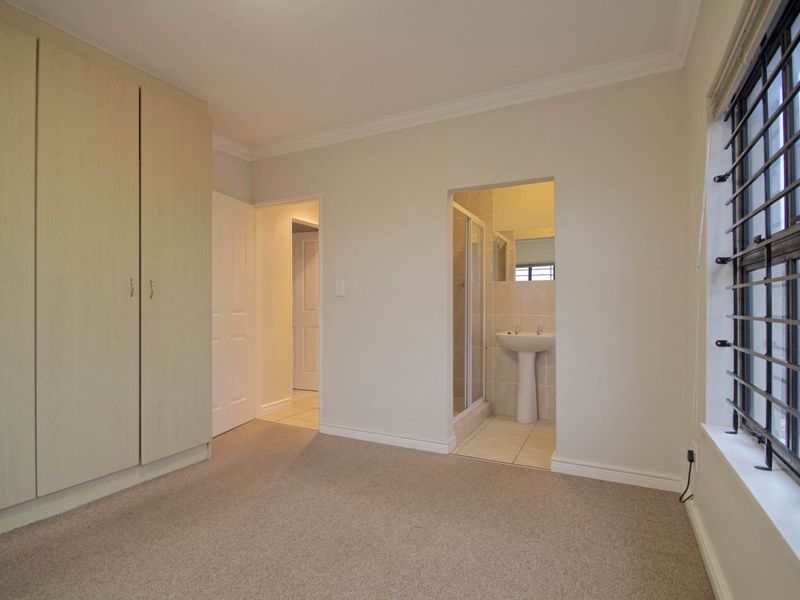 A clean, empty bedroom featuring built-in cupboards, carpeted flooring, and an attached en-suite bathroom with a shower and pedestal basin.
