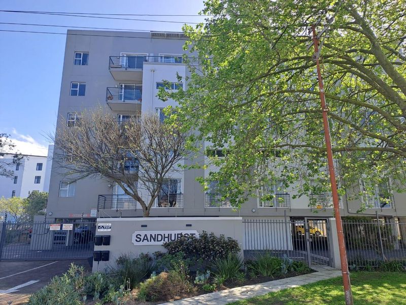 Exterior view of the Sandhurst apartment complex featuring a secure gated entrance, paved driveway, and multi-level balconies.