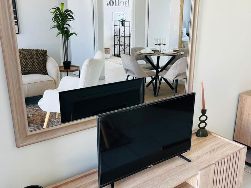 A bright living area featuring neutral tiled flooring and a large decorative wall mirror reflecting the adjacent dining space.