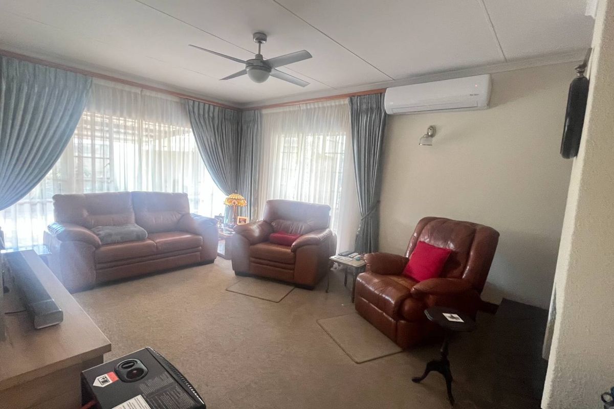 A comfortable living room featuring a ceiling fan, wall-mounted air conditioning unit, and large windows with curtains.