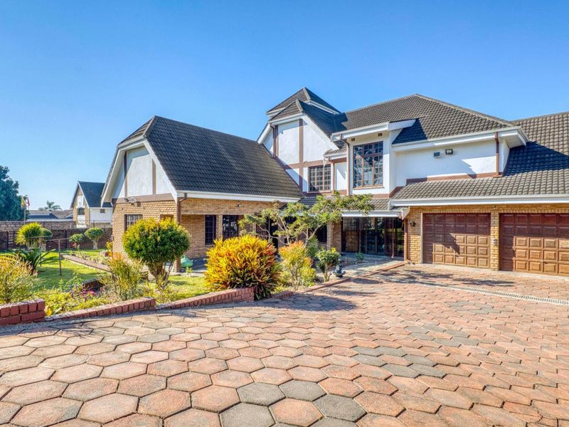 Front view of a well-maintained double-story residence featuring a brick facade, tiled roof, double garage, and a paved driveway set within a landscaped garden.