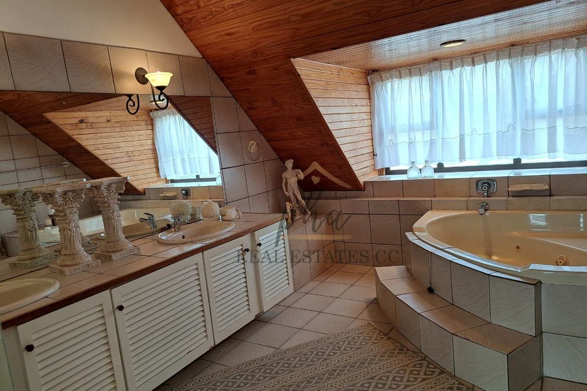 Spacious bathroom featuring a built-in corner jetted tub, dual vanity with integrated sinks, and distinctive wood-paneled vaulted ceilings.
