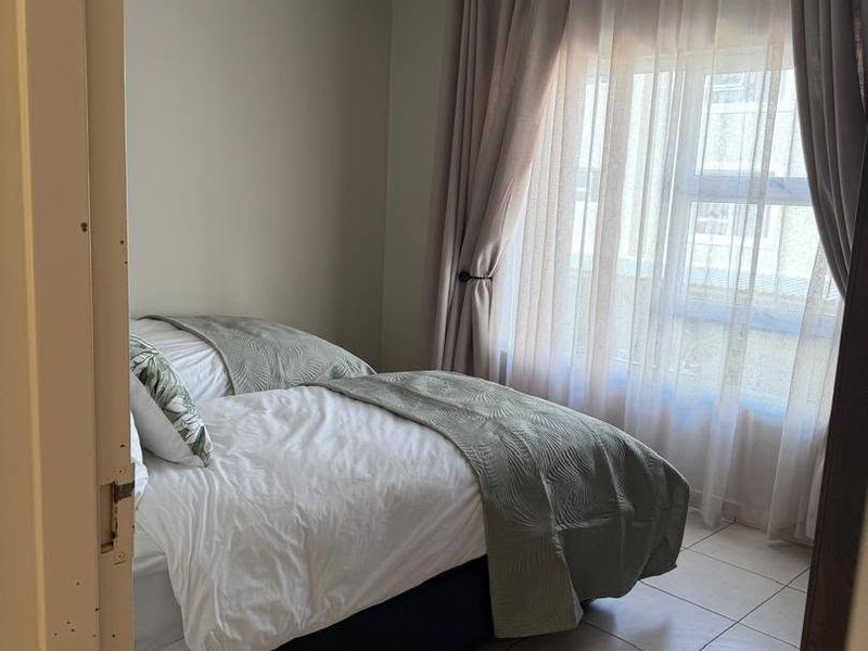 A bedroom featuring tiled flooring, a tongue and groove ceiling, and a large window with curtain tracks.
